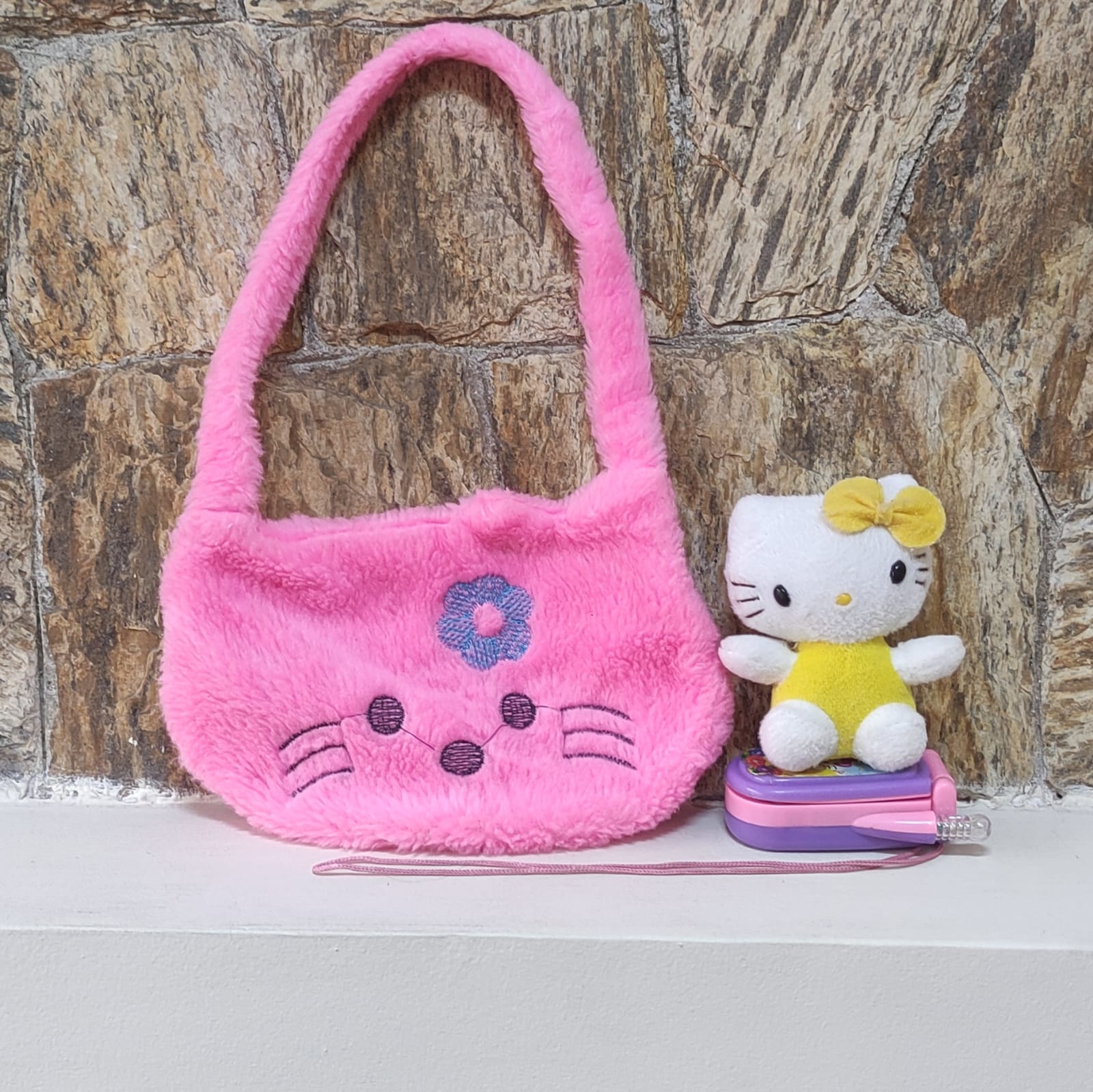 Kit contendo três itens da Hello Kitty dos anos 2000: uma bolsinha, uma mini pelúcia e um celular de brinquedo.